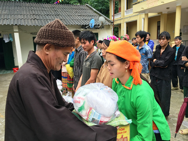 Trưởng đoàn từ thiện (người đội mũ, bên trái) tặng quà cho các hộ dân nghèo của xã Sơn Vĩ. 