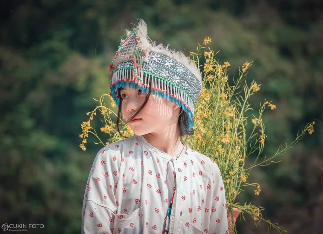 Nét mặt trong trẻo và sau lưng là những bó hoa rừng