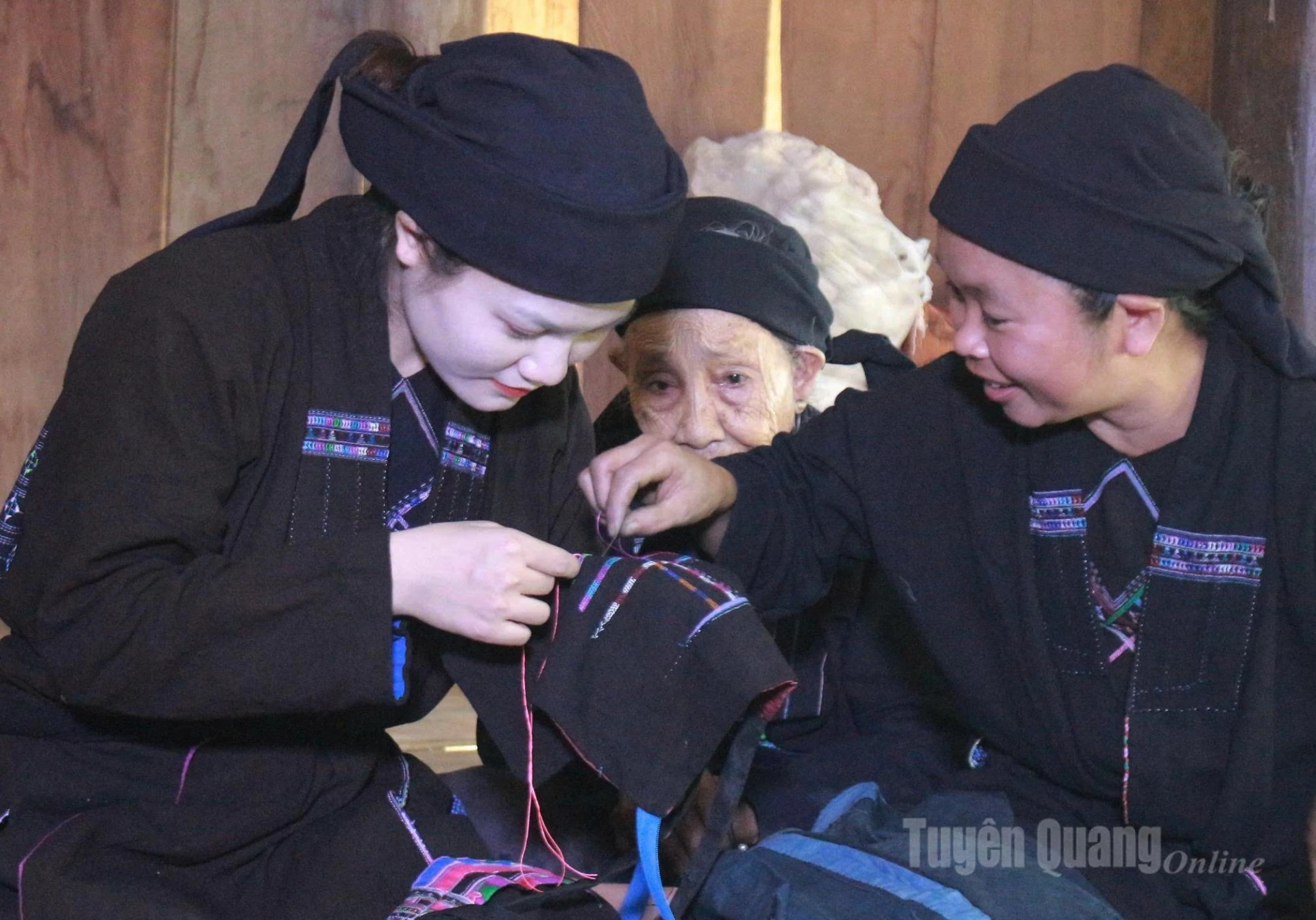 An artisan carefully instructs young La Chi women in embroidering patterns on traditional garments.
