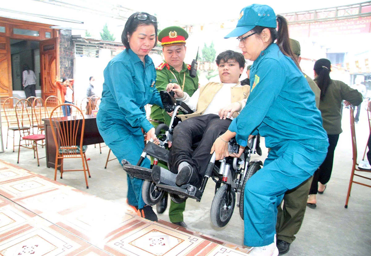 Lực lượng chức năng hỗ trợ người khuyết tật tham gia bỏ phiếu tại khu vực bỏ phiếu số 33, Nhà văn hóa tổ 9, 10, phường Minh Xuân. Ảnh: Mai Dung.