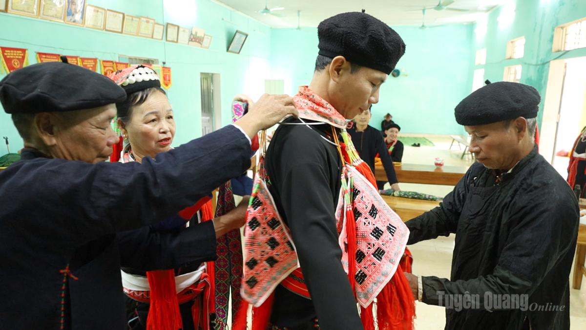The groom’s attire is simpler, consisting of a traditional garment with modest embroidered patterns and a fabric hat, also decorated with embroidery.