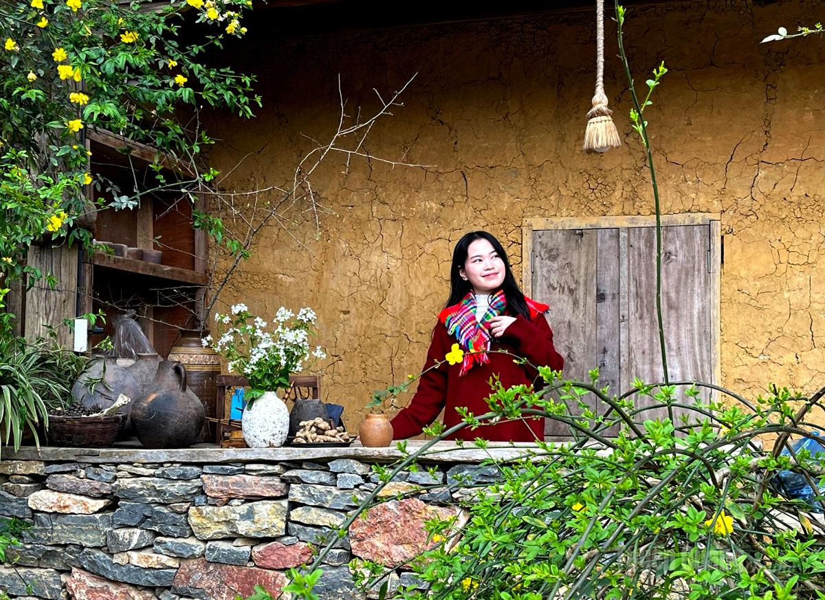 Visitors pose beside the porch of a traditional rammed-earth house in Lo Lo Chai Village, where bright yellow flower trellises and the rustic setting create an attractive check-in spot.