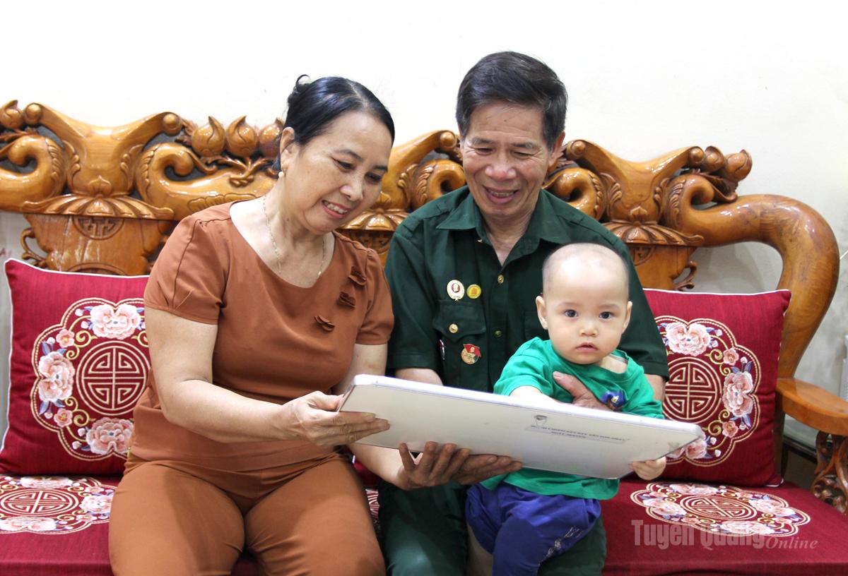 Cựu chiến binh Nguyễn Thế Liêm cùng gia đình xem lại bức ảnh Cờ giải phóng tung bay trên sân bay Tân Sơn Nhất, ngày 30/4/1975.