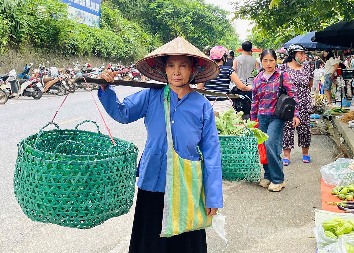 Bà cụ dân tộc Tày gánh những chiếc làn nhựa do chính tay mình đan, chậm rãi bước vào chợ phiên – hình ảnh thân quen và đầy chất quê giữa núi rừng.