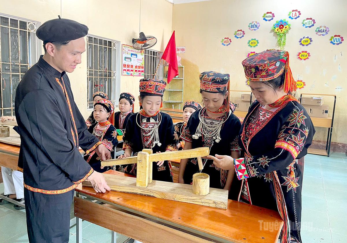 Giáo viên, Tổng phụ trách Đội Nguyễn Đình Kỷ  cùng gaio viên Phân hiệu Đá Bàn, trường Tiểu học Y Bằng, xã Phú Lâm hướng dẫn học sinh tìm hiểu mô hình cối giã gạo của đồng bào dan tộc thiểu số.