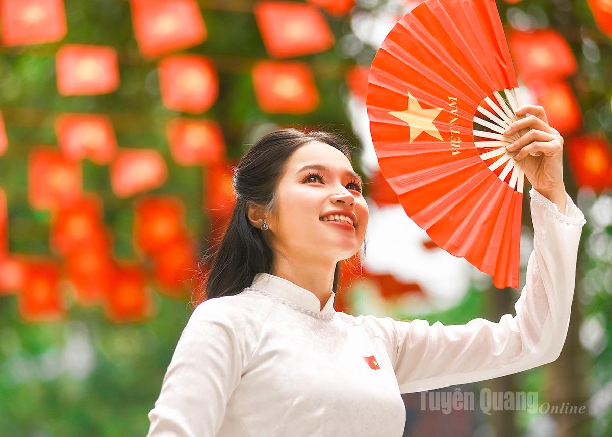 Người dân trong trang phục áo dài trắng truyền thống rạng rỡ chụp ảnh lưu niệm bên hàng cờ đỏ, hòa chung không khí hân hoan chào mừng Đại hội.