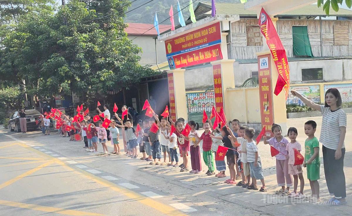 Các em học sinh trường Mầm non Hoa Sen, xã Phương Độ chào đón đoàn xe di chuyển hài cốt liệt sĩ. Ảnh: Thanh Phúc
